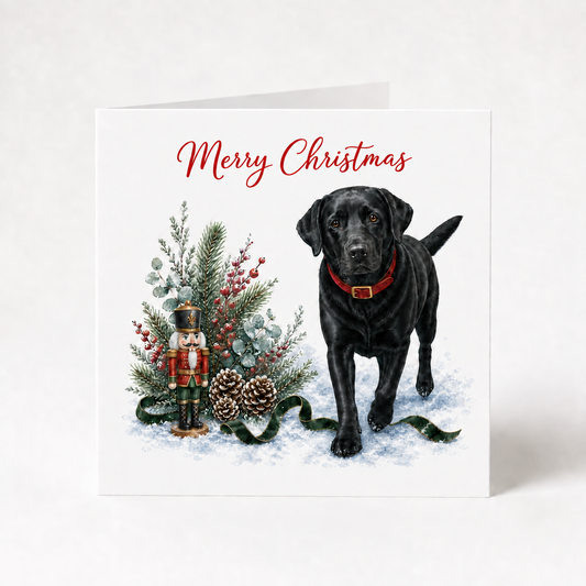 A square Christmas greeting card featuring a black Labrador retriever standing in snow beside a decorated Christmas tree, nutcracker, pinecones, and a green snake, with 'Merry Christmas' written in red script at the top.