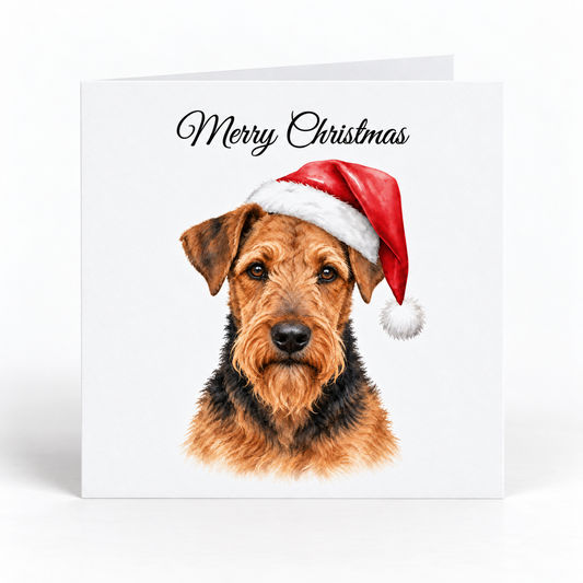 A square white Christmas greeting card with the words 'Merry Christmas' in black script at the top and an illustrated Airedale terrier dog wearing a red Santa hat on the front, shown against a light gray background.